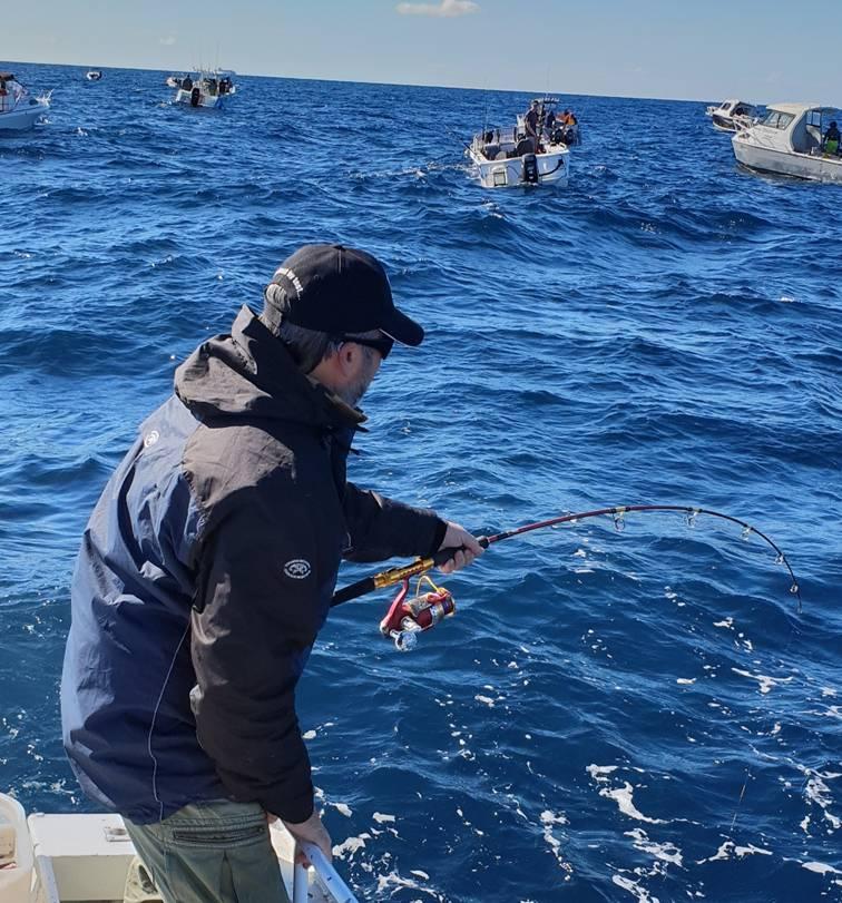 Angler fighting a kingfish on jigging tackle with boats nearby at Twelve Mile Reef